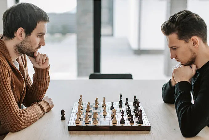 Two men playing chess at a table with a blurred indoor background