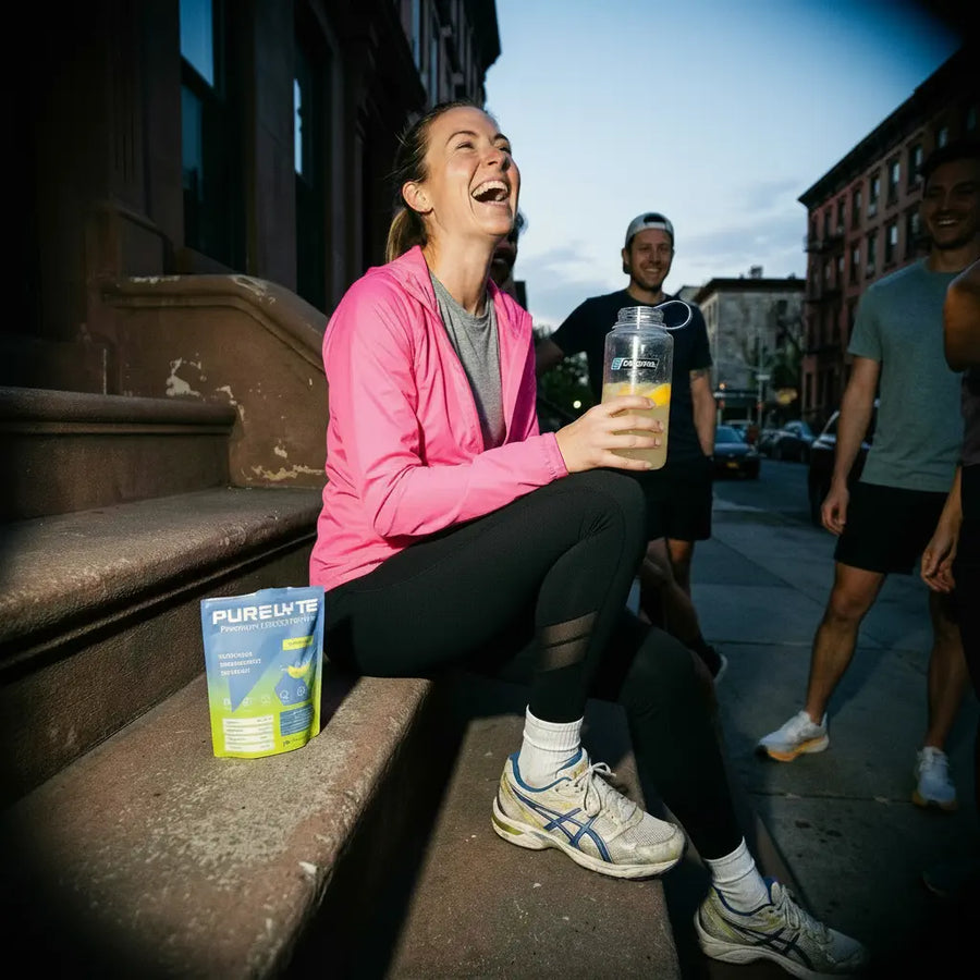 Person sitting on a step with a drink and Purelyte water container, with people and urban background